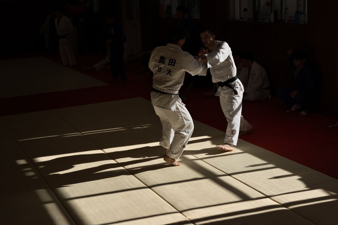 Dynamische Judo-Trainingsszene in einem japanischen Dojo. Eingefangen in einem Moment des Kontrasts zwischen Licht und Schatten auf dem Tatami.